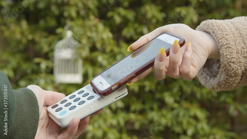 Contactless payment with a smart phone outside an independent cafe female hand