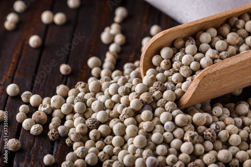 white peppercorns in wooden scoop on rustic background