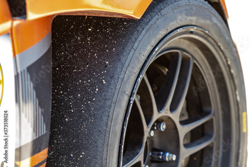 Εκτύπωση καμβά A sports car wheel with a worn slick tire with adhered asphalt close-up and orange parts of the car in the sun