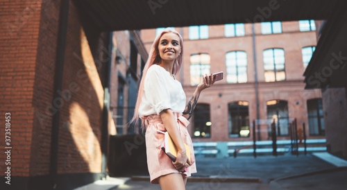 Принти на полотні Cheerful female student 20s with education textbook and smartphone device standi