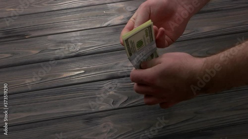 Bundle of dollars falling on wooden table. Male hand taking dollars bundle. Bribery concept. photo