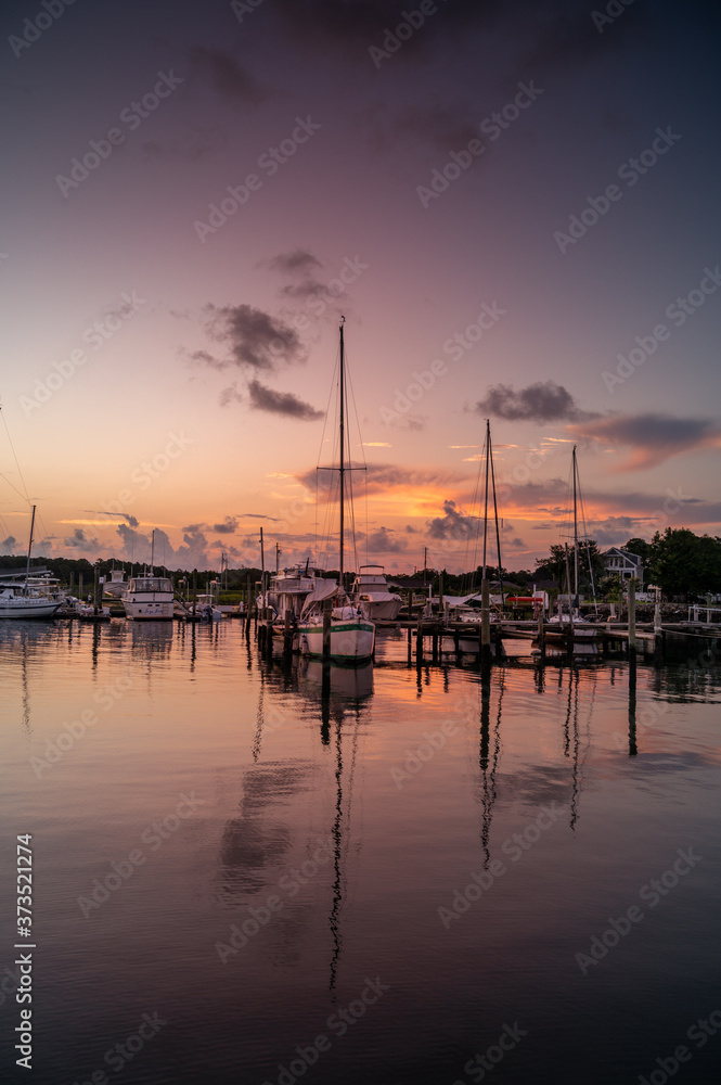 Predawn at the marina with sailboats at the dock in calm water.