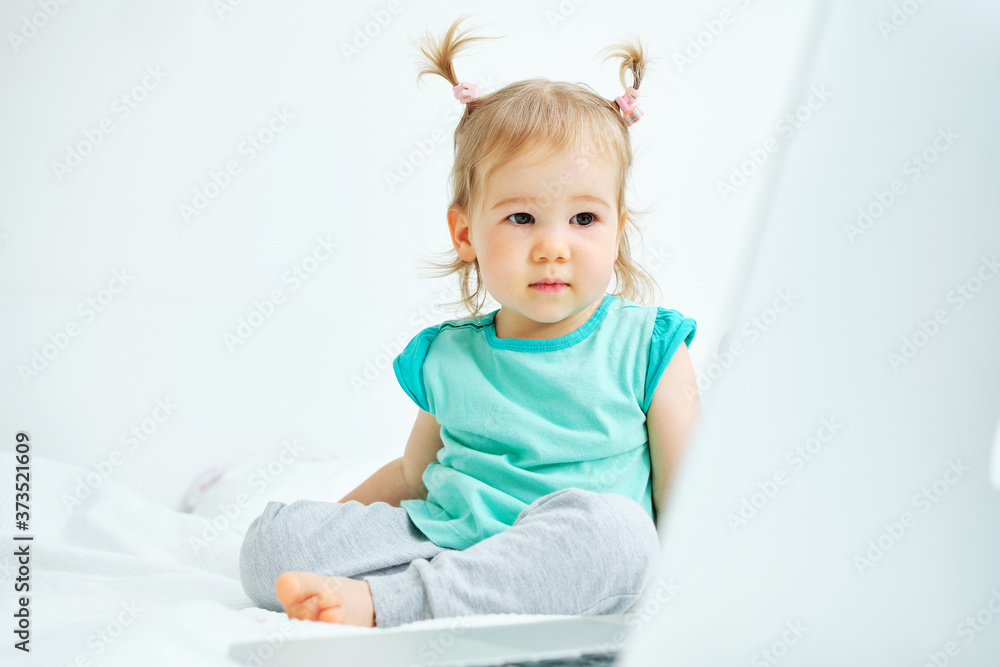 Caucasian kid sitting on bed and looking at laptop Caucasian kid sitting on bed and looking at laptop