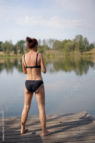 a woman in a bikini throws a fishing pole from a jetty on a lake