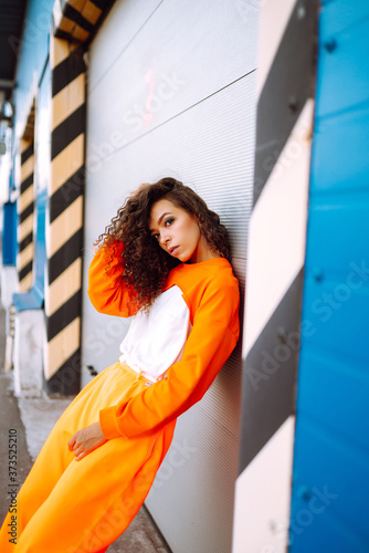 Portrait of stylish woman with curly hair in an orange suit. Young African American woman hip-hop dancer at sunset. Sport, dancing and urban culture concept. 