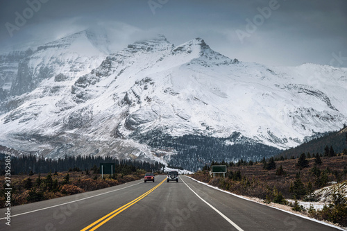 Car on highway and snowy mountain range in gloomy at Icefields Parkway