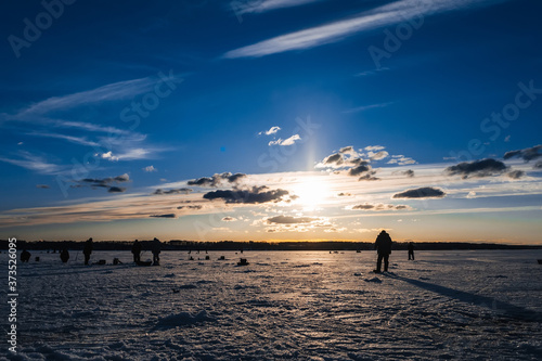 Winter fishing. Silhouette of fishermen catching fish on the icy surface of the river