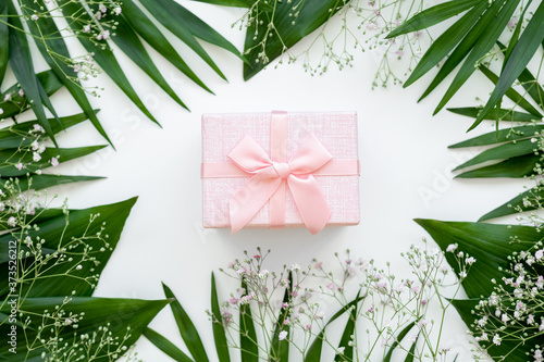 Holiday present. Floral composition. Pink gift box with ribbon bow in green leaf frame isolated on white. Natural arrangement. Festive background.