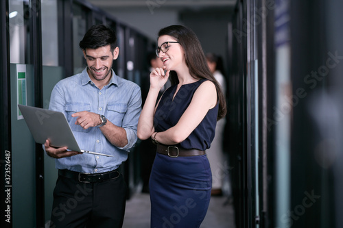 Two office employees are discussing about work outside of a meeting room and looking happily with their results.