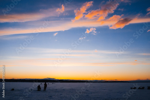 silhouettes of fishermen on winter fishing on the ice of the river