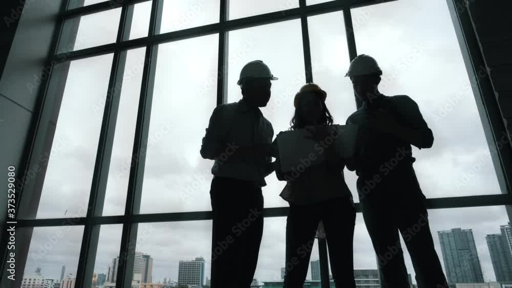 Silhouette of Asian group Architect and engineer construction workers on plans with a blueprint while working for teamwork. Architects discussing business plans. Silhouette of Asian group Architect and engineer construction workers on plans with a blueprint while working for teamwork. Architects discussing business plans.