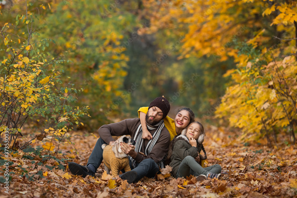 Young happy family with dog in leaves on autumn day