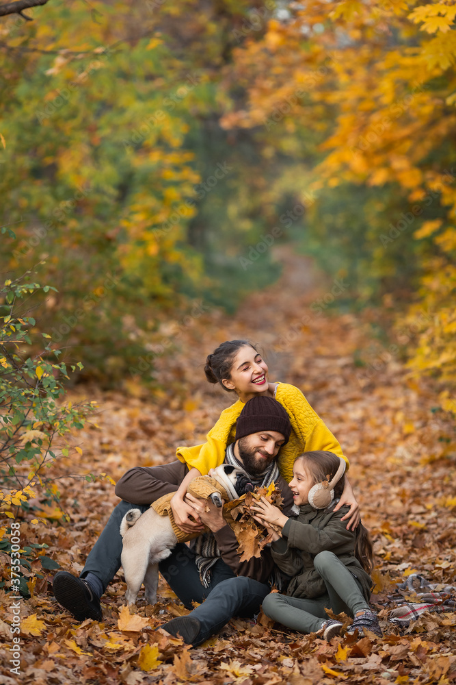 bearded dad with daughters and a dog in the leaves in autumn in the park