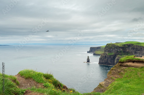 Cliff of Moher, county Clare, Ireland. Famous Irish tourist destination. Small airplane flying by. Cloudy sky, nobody