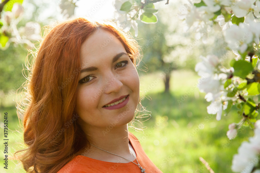 Portrait of a red-haired girl walking in an apple orchard in an orange dress Portrait of a red-haired girl walking in an apple orchard in an orange dress
