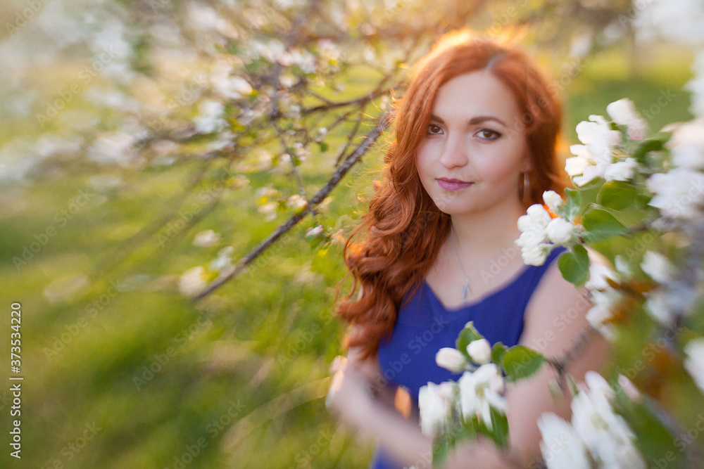 Tiltshift Portrait of a red-haired girl walking in an apple orchard in an blue dress Tiltshift Portrait of a red-haired girl walking in an apple orchard in an blue dress