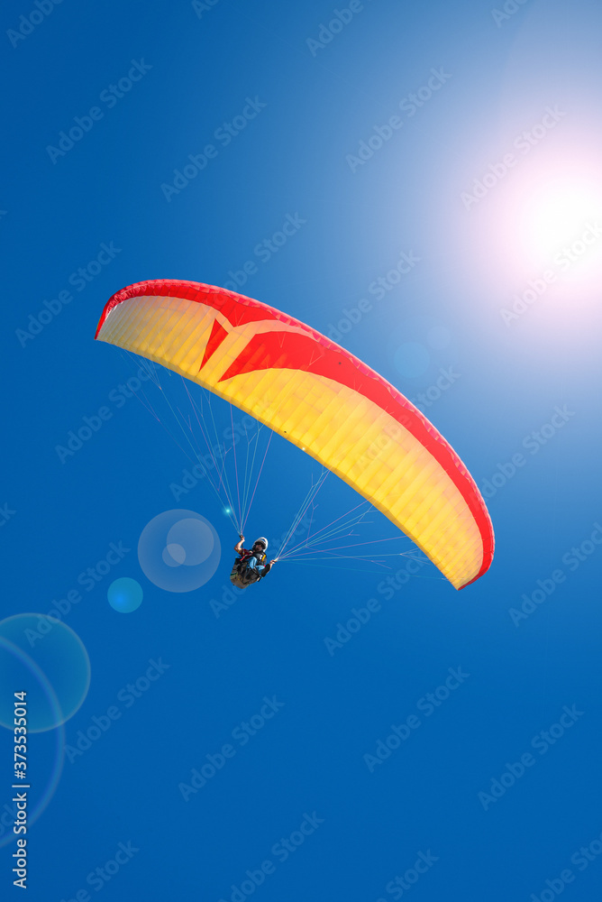 Beautiful yellow and red paraglider flying in blue sky with lens flare effect and copy space, details Beautiful yellow and red paraglider flying in blue sky with lens flare effect and copy space, details