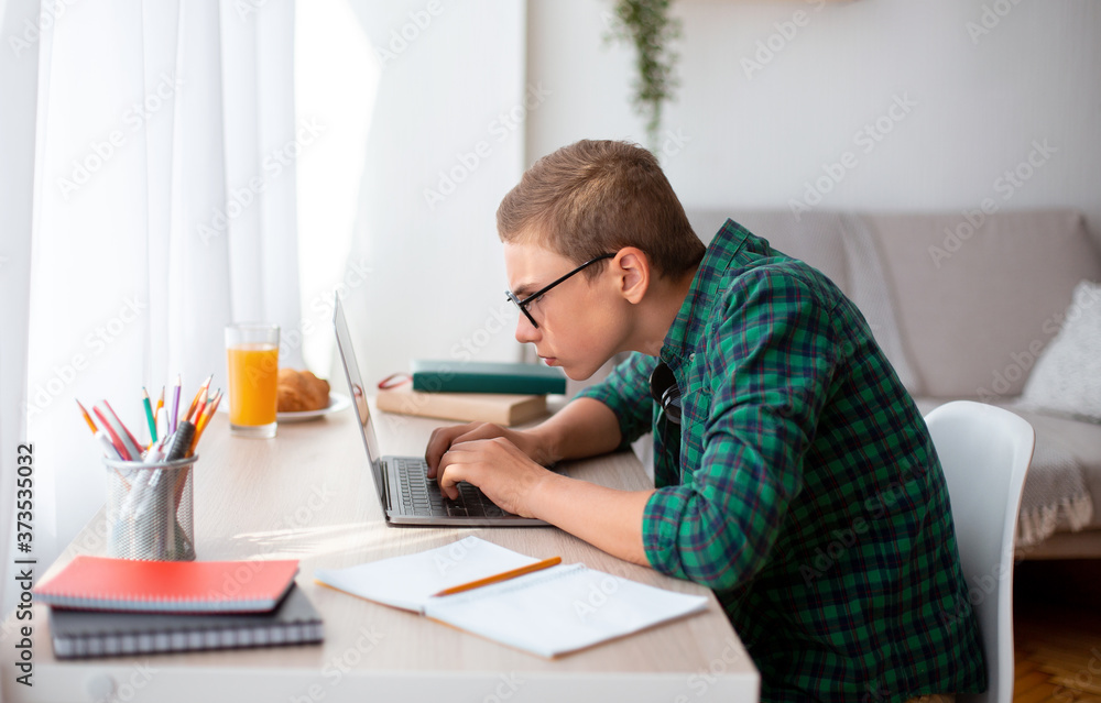 Concentrated nerd boy using laptop, working on project at home