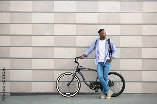 Happy African American man with bicycle near brick wall in city, space for text