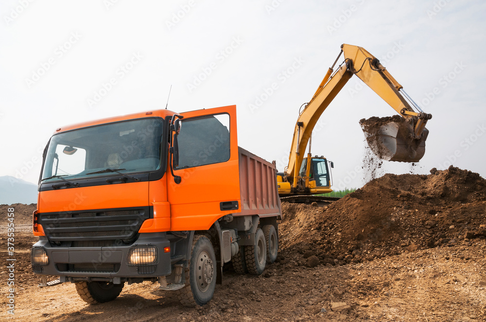 Loading of earth soil into the body of a cargo dump truck by an excavator bucket Loading of earth soil into the body of a cargo dump truck by an excavator bucket