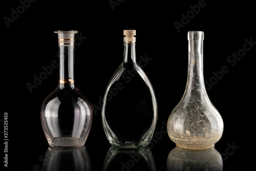Glassware on a black isolated background. Decanters of various shapes. A group of transparent items. The reflection under the objects. Old household items. Fragile dishes. Liquid containers.