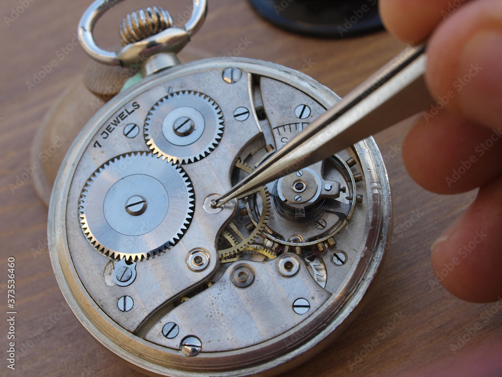 vintage pocket watch under repair, with exposed mechanism, watchmaker taking a small gear with tweezers