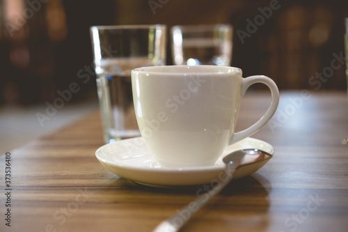 white cup of coffee on the table and two glass of water, cup of tea in a white cup with spoon at the cafe, soft focus
