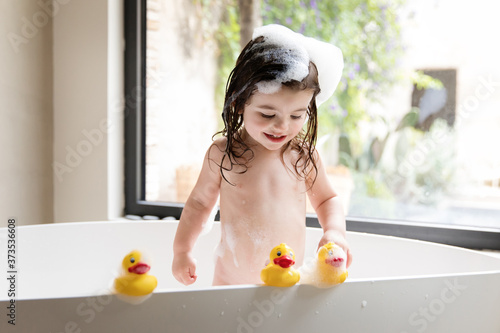 Smiling toddler girl playing with rubber ducks in bathtub