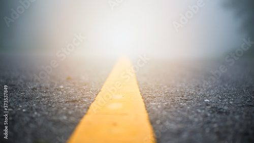 Selective focus yellow line on asphalt road with misty blurred background.