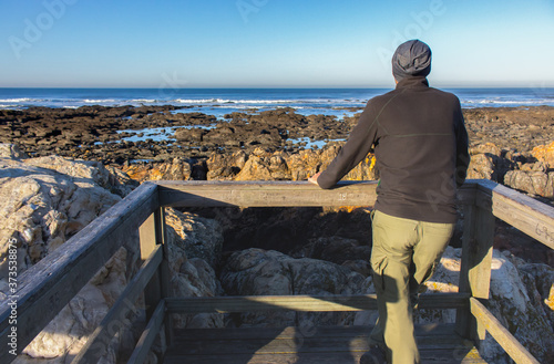 Lonely man from the back on the beach of Atlantic ocean, Portugal. Quiet morning on Atlantic ocean coast. Seascape with cliffs. Travel and freedom concept. Tourist on seashore. Summer relaxation. 