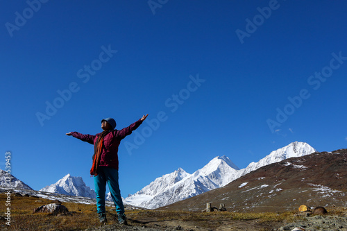 A young lady with red jacket on the top of Kunzum Pass in front of snow peaks on The Himalays in India