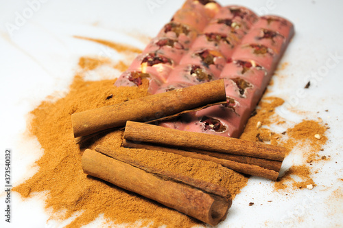 Bar of pink chocolate with raisins and fruits on a background of cinnamon sticks close up