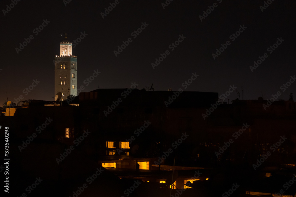 Koutoubia mosque minaret at night in Marrakech with the silhouette of the houses of the city at its feet