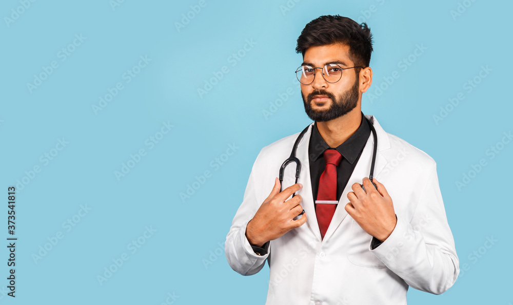 Cute Indian / Asian doctor wearing glasses with stethoscope, tie and white coat on light blue background. Cute Indian / Asian doctor wearing glasses with stethoscope, tie and white coat on light blue background.