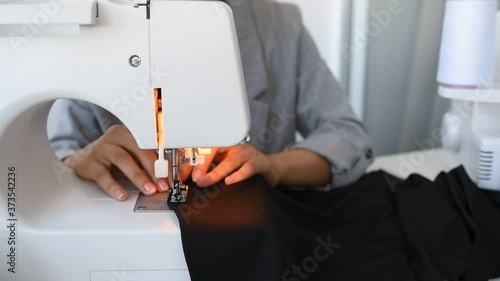 Young woman tailor is sewing on sewing machine in her mini workshop.