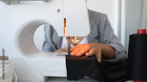 Young woman tailor is sewing on sewing machine in her mini workshop.