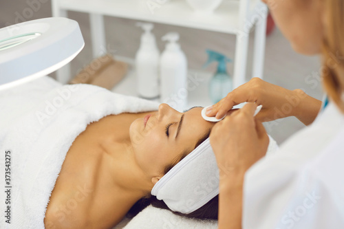Cosmetologist cleaning woman facial skin with cotton pads before beauty treatment