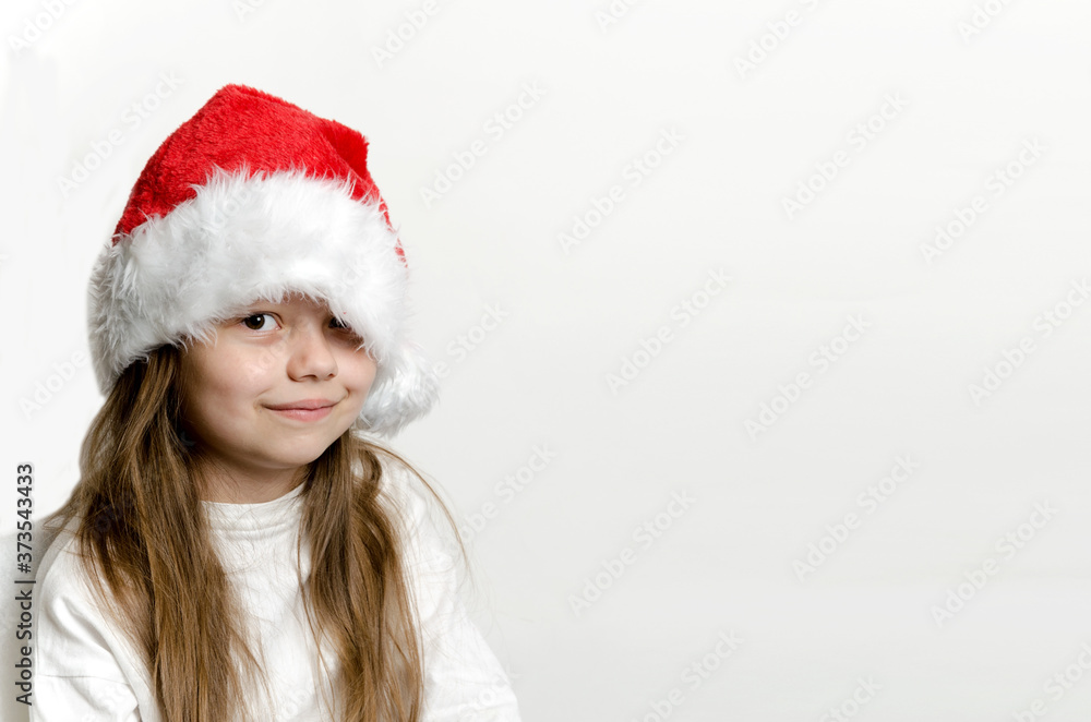 Smiling child, girl in Santa Claus hat on light background with copy space Smiling child, girl in Santa Claus hat on light background with copy space