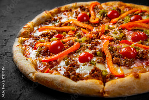 Pizza with Mozzarella cheese, Bolognese sauce, minced meat, pepper, tomato, bacon and vegetables. Italian pizza on Dark grey black slate background
