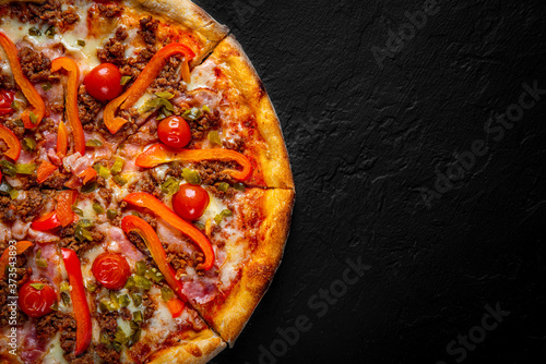 Pizza with Mozzarella cheese, Bolognese sauce, minced meat, pepper, tomato, bacon and vegetables. Italian pizza on Dark grey black slate background