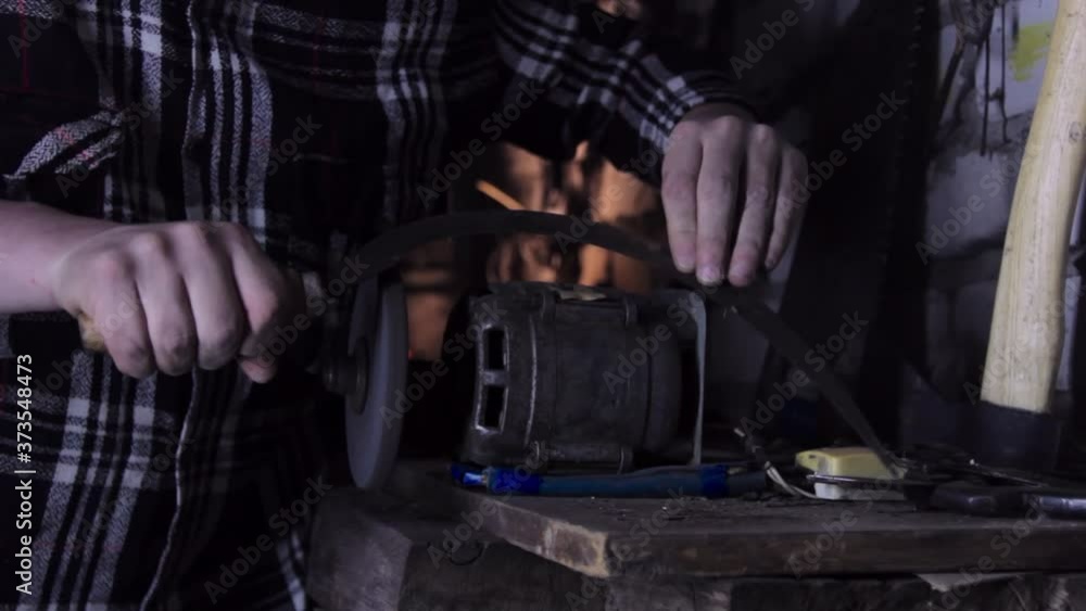 A man sharpens a sickle on a grinder sharpener close-up A man sharpens a sickle on a grinder sharpener close-up