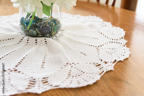 Toalha de crochê na cor branca com um vaso contendo pedras e flores em um fundo de madeira photo