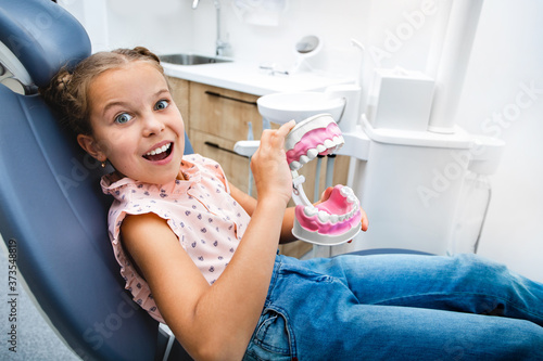 Children's teeth care. An emotional little girl playing with a jaw model, she sitting in the dentist's chair. My teeth is healthy