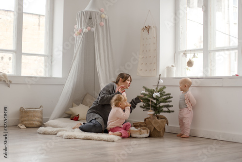 Two cute little baby girls play with their mom in a bright minimalistic children's room.