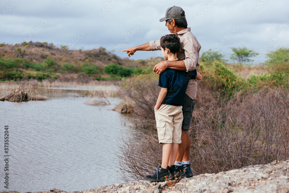 Latin grandfather with his grandson enjoying the natural landscape of a lake. Concept of