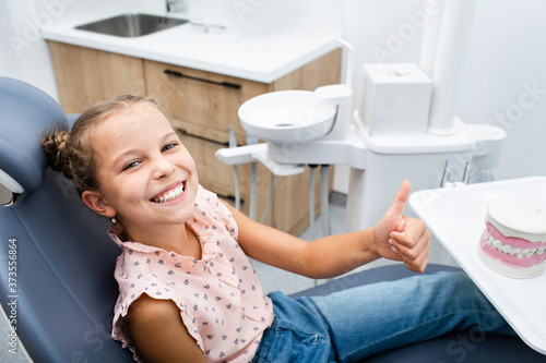 Very happy smiling girl sitting on a dental chair and showing thumbs up.
