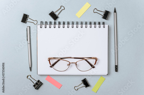 Flat layout of office workplace with stationery. Blank stickers with place for text, pencils, glasses, notebook, binder clips and pushpins isolated on white and blue background. Office supplies set.