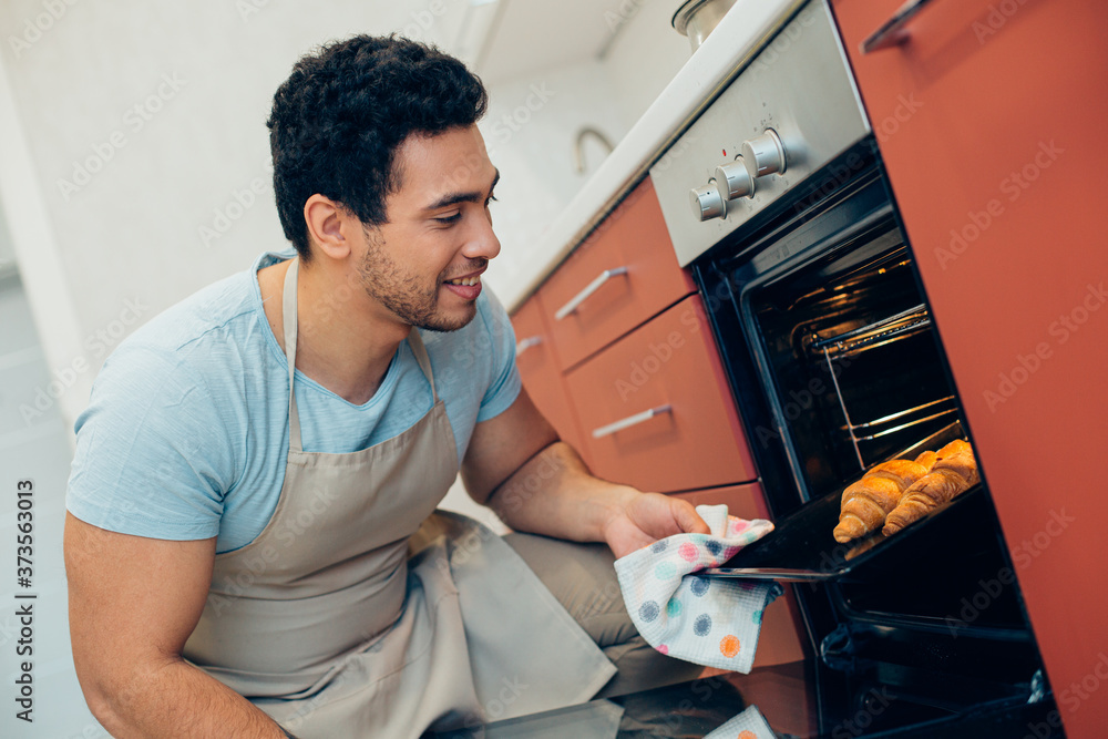 Obraz premium Satisfied male cook looking at his croissants in the oven