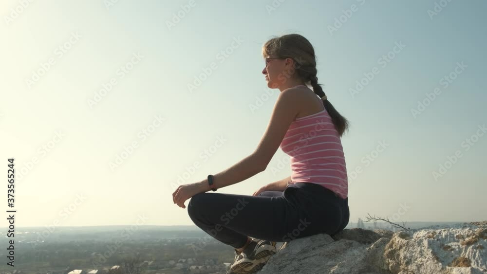 Young relaxed woman sitting outdoors on a big stone enjoying warm summer day. Girl meditating and relaxing on nature at sunset. Young relaxed woman sitting outdoors on a big stone enjoying warm summer day. Girl meditating and relaxing on nature at sunset.