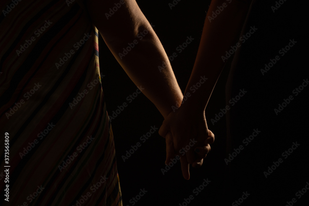 Silhouette of lesbian couple holding hands in studio with black background